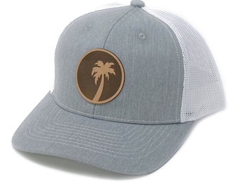 May include: A gray and white trucker hat with a brown leather patch featuring a palm tree silhouette.