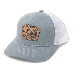 Puede incluir: Una gorra de camionero gris y blanca con un parche de cuero marr&oacute;n que dice "I'd Rather Be Outside" y presenta una escena de monta&ntilde;a.