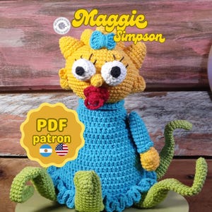 Puede incluir: Muñeca Maggie Simpson hecha a mano con ganchillo, con cabeza amarilla, lazo azul, ojos grandes y chupete rojo. La muñeca lleva un vestido azul y tiene piernas verdes en forma de tentáculos. El texto "Maggie Simpson" está arriba.