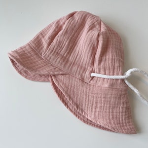 May include: A pink sun hat with a white drawstring. The hat is made of a soft, textured fabric.