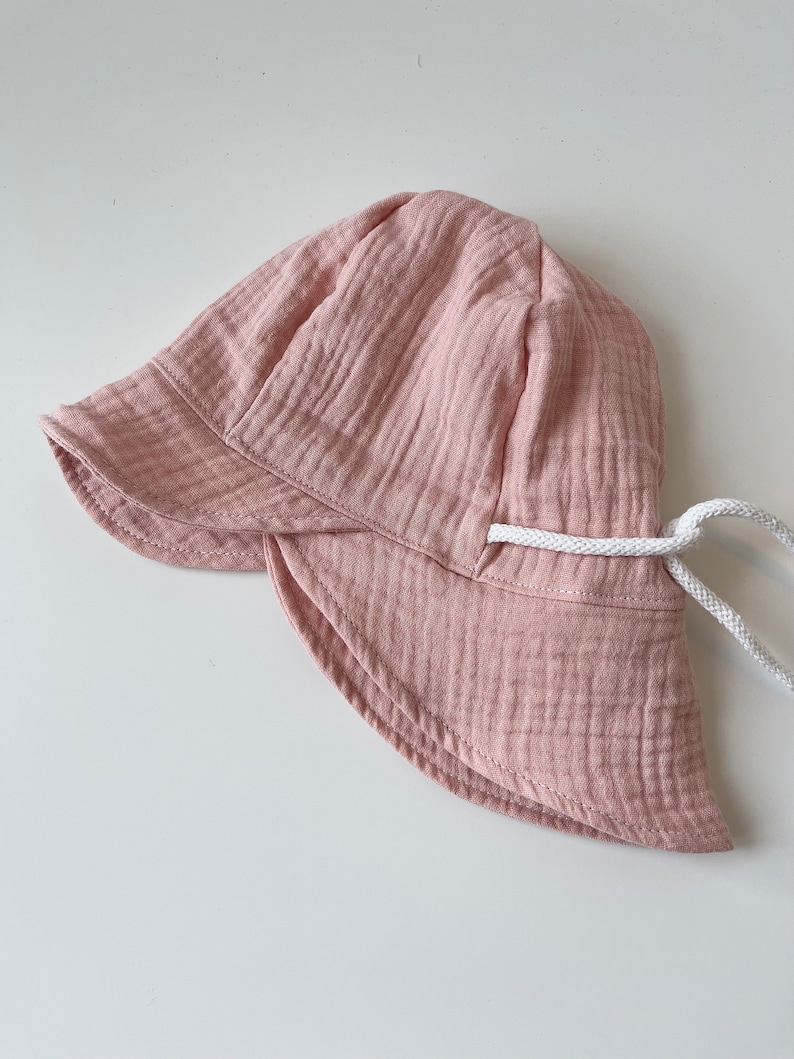 May include: A pink sun hat with a white drawstring. The hat is made of a soft, textured fabric.