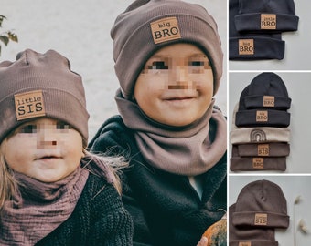 May include: Two children wearing brown knit beanies with the words "little sis" and "big bro" on them. The children are wearing matching brown knit scarves. The image also shows a variety of beanies with different color combinations and the same text.