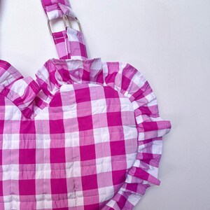 May include: Pink and white gingham heart-shaped bag with a ruffled trim and a silver buckle strap.