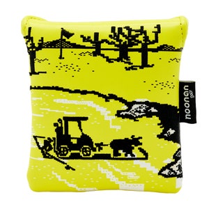 Puede incluir: Bolsa amarilla para bolas de golf con un diseño pixelado en blanco y negro de un campo de golf, un carrito de golf y árboles. La bolsa tiene una etiqueta negra con la palabra "noonan" y la palabra "golf" impresa en ella.