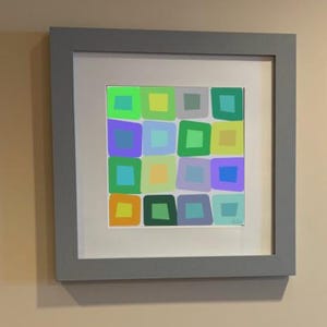 May include: A square framed wall art piece featuring a grid of sixteen hand-drawn style squares in various colors including lime green, yellow, purple, blue, orange, and gray. The artwork is set within a white mat and a solid gray frame.