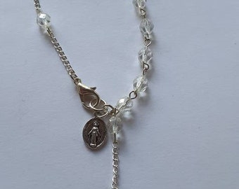 May include: A silver chain bracelet with clear crystal beads and a silver charm with a cross and a religious image.