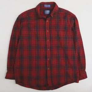 Könnte beinhalten: Ein rot-blau kariertes Button-Down-Hemd. Das langärmlige Hemd hat einen klassischen Kragen, eine Brusttasche und Knopfverschlüsse. Das Hemd ist aus einem weichen, gewebten Stoff gefertigt.