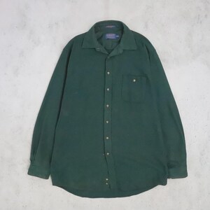 Pode incluir: Uma camisa de manga comprida com botões num tom verde floresta escuro sólido. A camisa apresenta um colarinho padrão, um bolso único no peito do lado esquerdo, uma carcela frontal completa com botões verdes a condizer e uma etiqueta no colarinho.