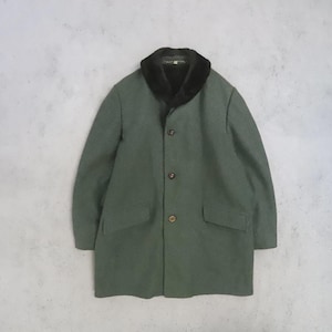 May include: A sage green coat featuring a dark brown faux fur shawl collar, long sleeves, and a front button closure with three visible buttons. The garment includes two horizontal flap pockets on the lower front section and a straight hemline.