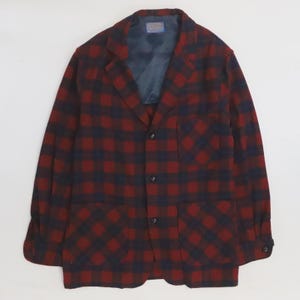 Puede incluir: Una blazer a cuadros rojos y azul marino con cierre de dos botones, dos bolsillos delanteros y solapa con muescas. La blazer tiene un forro azul oscuro y una etiqueta en el interior. La chaqueta está hecha de una tela gruesa y tejida.