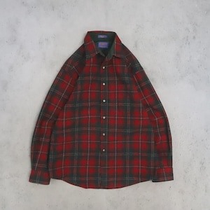 Può includere: Una camicia a maniche lunghe con bottoni e un motivo a quadri rosso e verde scuro. La camicia presenta un colletto a punta, un'abbottonatura frontale e polsini con bottoni. Un'etichetta del marchio Pendleton è visibile sul colletto.