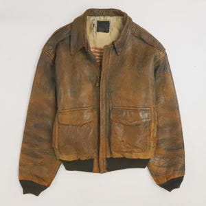 Puede incluir: Chaqueta bomber de cuero marrón con dos bolsillos delanteros y dobladillo y puños de canalé. La chaqueta tiene cuello y cierre de cremallera. El cuero tiene un aspecto envejecido con variaciones de color.