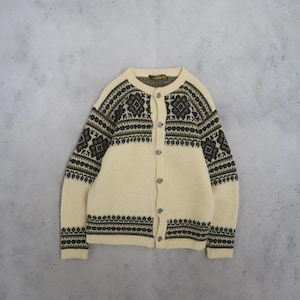 May include: A cream-coloured knit cardigan featuring a dark brown and olive green geometric pattern across the chest, shoulders, and sleeves. The garment has a round neckline, long sleeves, and a front button closure with five circular buttons.