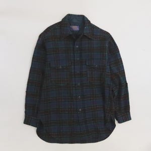 Peut inclure: Une chemise à carreaux à manches longues dans les tons bleu marine, vert et bordeaux. La chemise comporte deux poches de poitrine et une fermeture boutonnée sur le devant. Le tissu a un aspect doux et texturé.