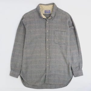 Puede incluir: Una camisa gris de manga larga con botones y un estampado de cuadros. La camisa tiene cuello abotonado, bolsillo en el pecho y forro beige en el cuello. La camisa está hecha de una tela suave y texturizada.