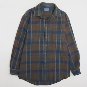 May include: A long-sleeve button-down shirt featuring a plaid pattern in shades of brown, dark blue, and grey. The shirt has a standard collar, a single chest pocket on the left side, and a buttoned front placket with a Pendleton brand label.