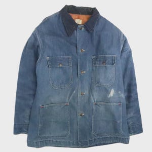 May include: A vintage blue denim jacket with a dark blue collar and four front pockets. The jacket has a button-up closure and a worn appearance, with some white marks on the front. The collar has a brown lining.