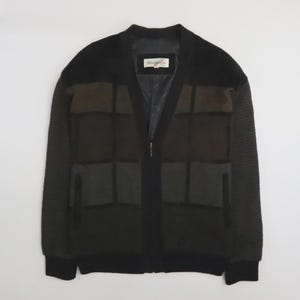 May include: A black zip-up jacket featuring a color-blocked grid pattern in shades of dark brown and charcoal gray. The garment has a V-neckline, long sleeves with a ribbed texture, two side pockets, and a label inside reading Modango.