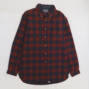 Puede incluir: Una camisa de manga larga con botones y un patrón de cuadros en rojo oscuro y azul marino. La camisa presenta un cuello puntiagudo, una tapeta frontal con botones claros y un dobladillo redondeado. La tela muestra un diseño de cuadros uniforme.