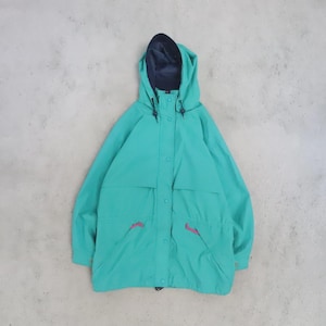 May include: A teal hooded jacket featuring a dark navy blue interior lining, a front zip closure concealed by a snap-button placket, long sleeves, and two front pockets accented with small, bright pink pull tabs on the zips.