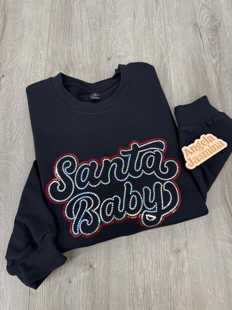 May include: Black sweatshirt with a red and white "Santa Baby" design made of rhinestones. The sweatshirt has long sleeves and a crew neck.