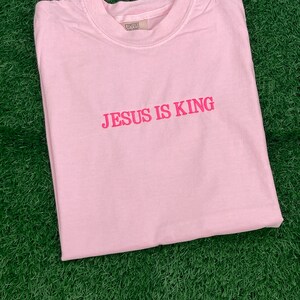 May include: A pink t-shirt with the text "JESUS IS KING" in pink lettering.