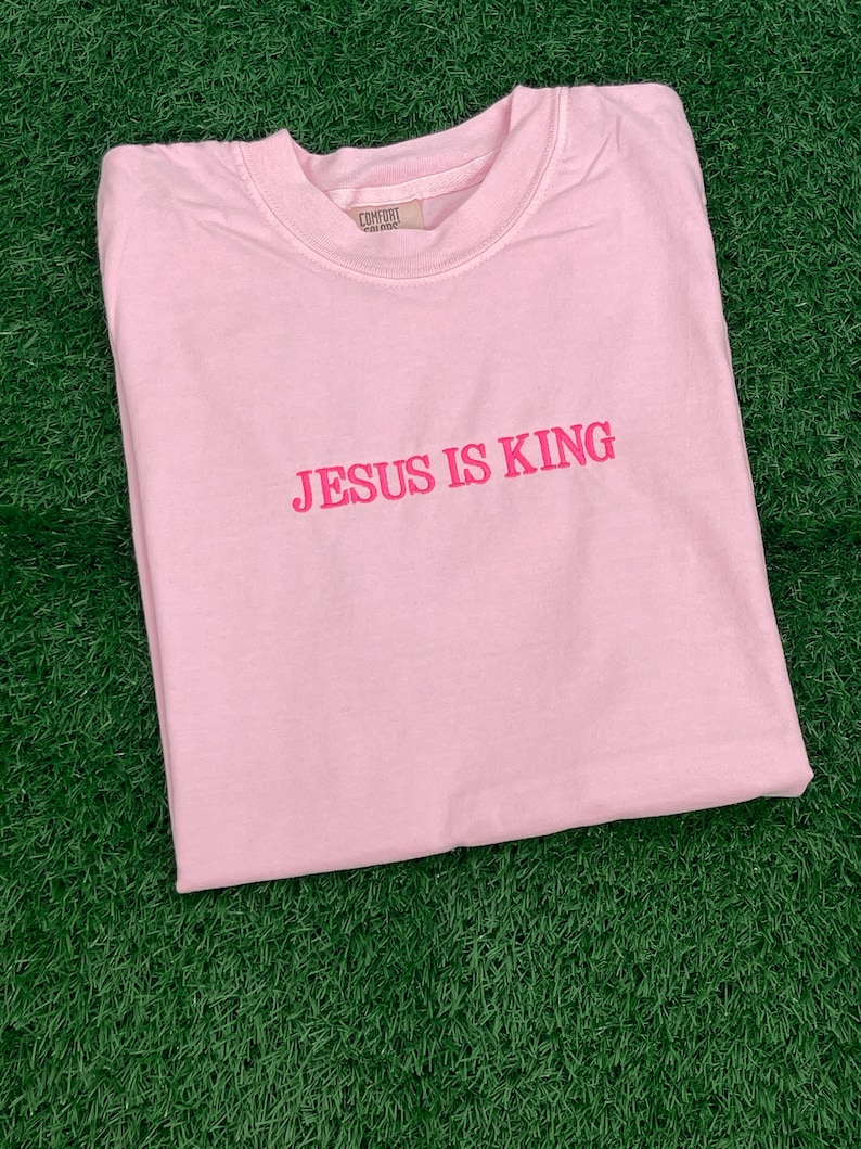 May include: A pink t-shirt with the text "JESUS IS KING" in pink lettering.