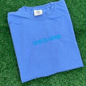 May include: A blue t-shirt with the text "GOD IS GOOD" embroidered in light blue on the front.