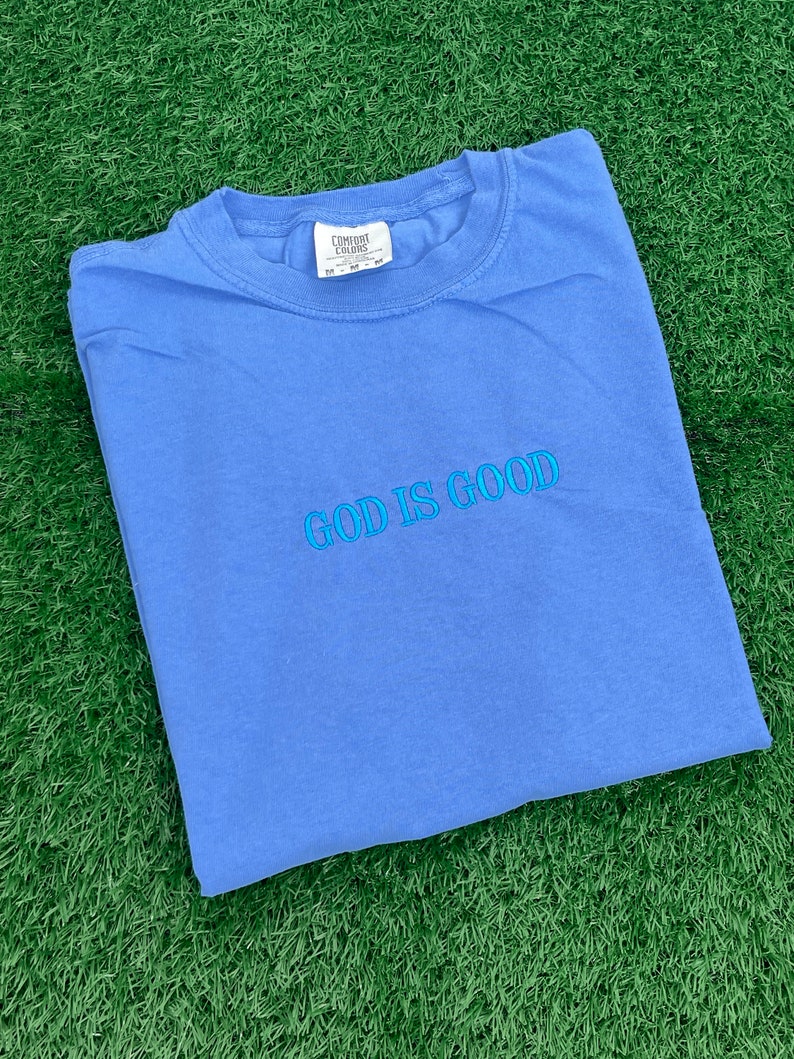 May include: A blue t-shirt with the text "GOD IS GOOD" embroidered in light blue on the front.