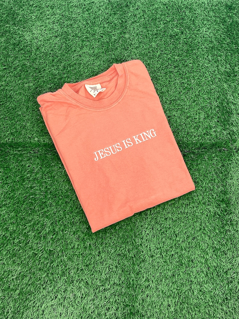 May include: A coral pink t-shirt with the text "JESUS IS KING" in white lettering.
