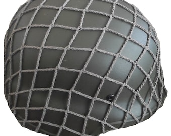May include: An olive drab military helmet with a tan net cover. The helmet has a rounded shape and a smooth surface. The net is made of thick, woven material and is secured over the helmet. A small, black rivet is visible on the side.