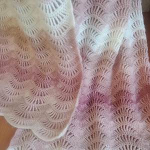 Peut inclure: Une couverture en crochet avec un motif ombré rose et blanc. La couverture est réalisée avec un point délicat et ajouré.