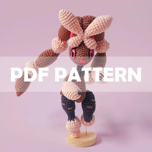 Könnte beinhalten: Gehäkelte Puppe in Braun-, Beige- und Rosatönen, mit großen Ohren und einem skurrilen Design. Die Puppe wird auf einem Holzständer präsentiert. Der Text "PDF PATTERN" ist auf dem Bild überlagert.