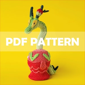 Puede incluir: Patrón de crochet para un dragón amigurumi verde y rojo con una flor en la cabeza. El patrón está disponible para descargar en PDF.