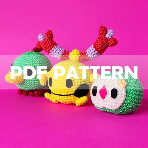 Puede incluir: Tres criaturas de ganchillo coloridas, verdes, amarillas y blancas, con detalles rojos y morados, sobre un fondo rosa brillante. La imagen incluye el texto "PDF PATTERN". Las criaturas parecen hechas a mano.