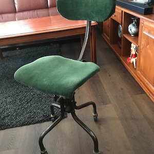 Op de afbeelding: Groene corduroy bureaustoel met een gebogen rugleuning en zitting. De stoel heeft een metalen frame met vier poten en kleine wielen. De stoel is ontworpen voor comfort en functionaliteit, geschikt voor een thuiskantoor of werkruimte.