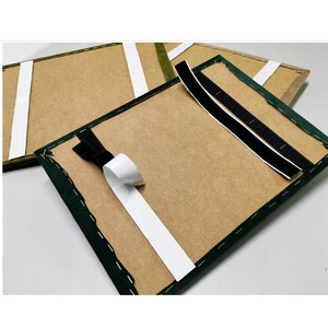 Könnte beinhalten: Zwei Stücke braunen Kartons mit grünen Stoffkanten. Ein Stück hat weißes und schwarzes Klettband auf der Rückseite befestigt. Das andere Stück hat schwarzes Klettband auf der Rückseite befestigt.