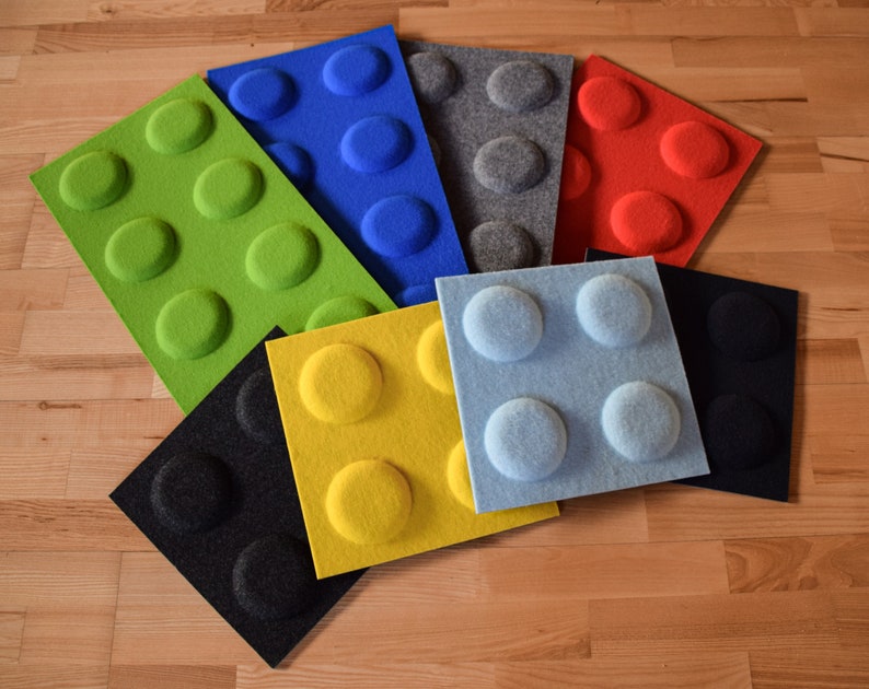 K&ouml;nnte beinhalten: Ein Set aus neun Akustikpaneelen in verschiedenen Farben, darunter Gr&uuml;n, Blau, Grau, Rot, Gelb, Schwarz und Hellblau. Jedes Panel hat ein erhabenes Muster aus Kreisen, das an einen Lego-Stein erinnert.