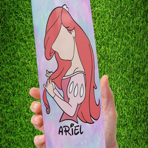May include: A pink and blue galaxy-themed tumbler with a cartoon image of Ariel from The Little Mermaid. The tumbler has the word "Ariel" written on it.