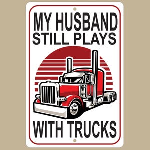 May include: White metal sign with red, white, and black text that reads "My Husband Still Plays With Trucks". The sign features a cartoon illustration of a red semi-truck with a white cab.