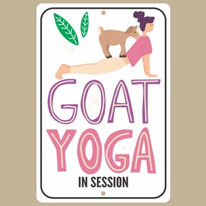 May include: A white rectangular sign with a black border features the words "GOAT YOGA" in pink and purple, with "IN SESSION" below. An illustration shows a person in a yoga pose with a goat on their back, and green leaves at the top.