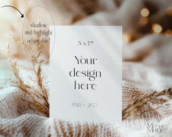 May include: A white card mockup with the text "5 x 7", "Your design here", and "PSD + JPG" on a beige knitted surface with dried grass. The card has a shadow and highlight effect that is adjustable.