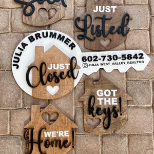 May include: Five wooden house-shaped signs with different real estate phrases. The signs are painted brown with black lettering. The phrases are "Sold", "Just Listed", "Just Closed", "Got the Keys!" and "We're Home!"