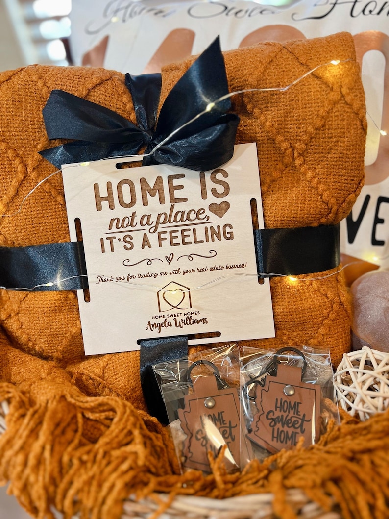 May include: A gift basket with a brown blanket, a wooden sign that says "HOME IS not a place, IT'S A FEELING", and two leather keychains that say "HOME Sweet HOME".