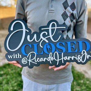 Pu&ograve; includere: Un cartello in legno nero con scritte 3D a strati. Il testo recita Just in corsivo bianco, CLOSED in stampatello blu e with @RicardoHarrisJr in corsivo bianco. Il cartello presenta una finitura scura e una tipografia in rilievo.
