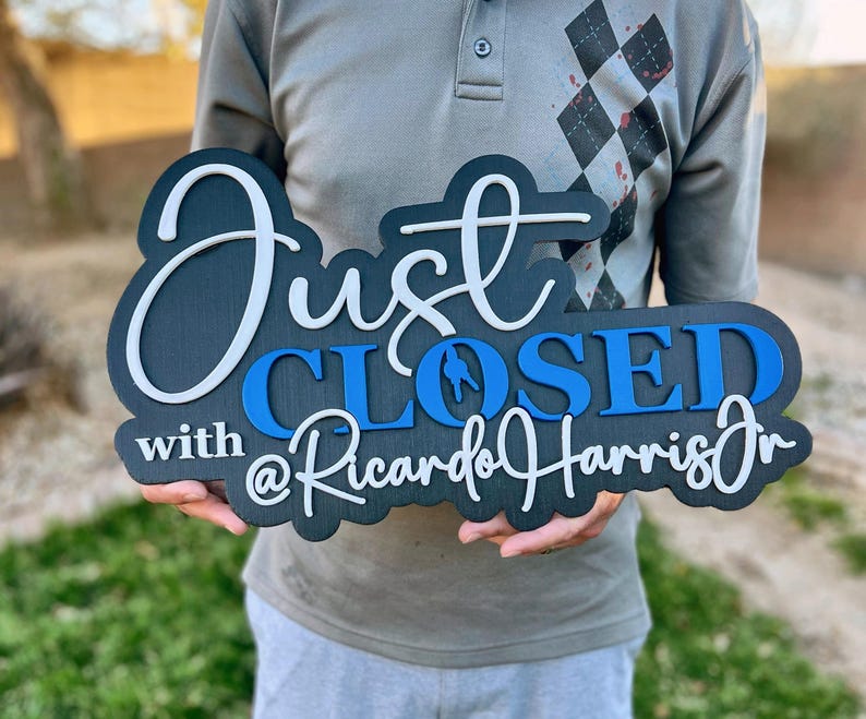 Pu&ograve; includere: Un cartello in legno nero con scritte 3D a strati. Il testo recita Just in corsivo bianco, CLOSED in stampatello blu e with @RicardoHarrisJr in corsivo bianco. Il cartello presenta una finitura scura e una tipografia in rilievo.
