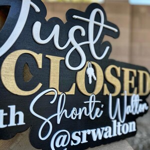 Pu&ograve; includere: Un cartello in legno nero con lettere 3D a strati. Il testo recita Just CLOSED with Shonte Walton @srwalton. La parola Just e il nome Shonte Walton sono in corsivo bianco, mentre CLOSED &egrave; in lettere dorate. Un'icona a forma di chiave bianca sostituisce la O.