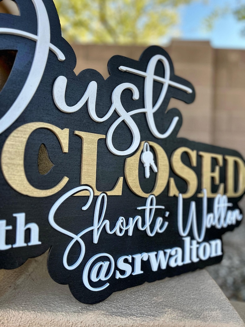 Pu&ograve; includere: Un cartello in legno nero con lettere 3D a strati. Il testo recita Just CLOSED with Shonte Walton @srwalton. La parola Just e il nome Shonte Walton sono in corsivo bianco, mentre CLOSED &egrave; in lettere dorate. Un'icona a forma di chiave bianca sostituisce la O.