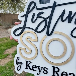 May include: White wooden sign with black lettering that reads "Listing Sold by Keys Real Estate". The letters are raised and the "Sold" is in gold.
