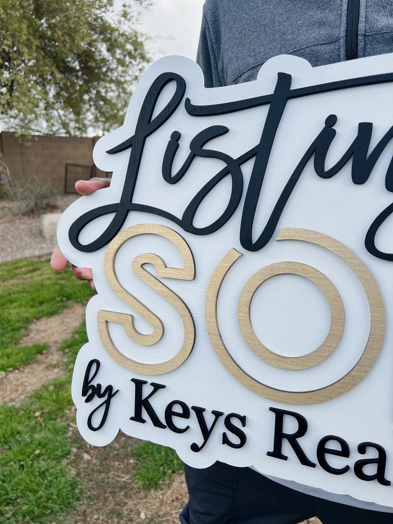May include: White wooden sign with black lettering that reads "Listing Sold by Keys Real Estate". The letters are raised and the "Sold" is in gold.